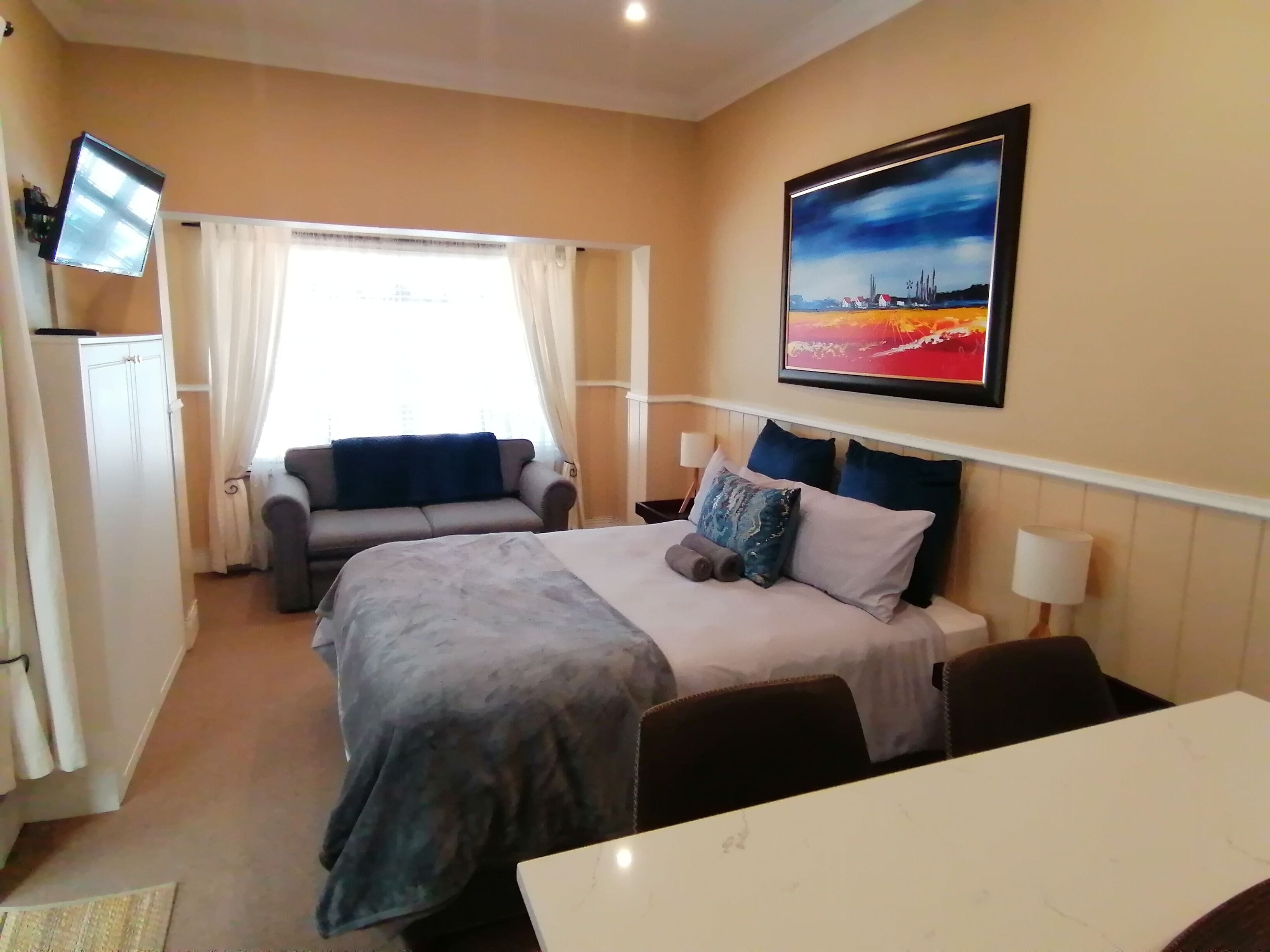 A hotel room with a bed, a sofa, a TV, and a painting on the wall.