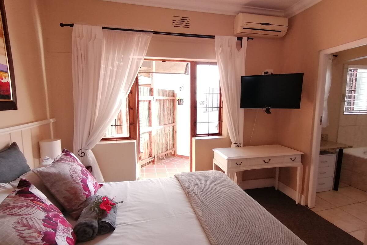 A bedroom with a bed, a desk, a TV, and an air conditioning unit.