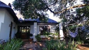 A house with a thatched roof, a paved pathway, and a hanging hammock. - Beulah Lodge (Cape Town)