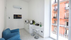 A modern kitchen with white cabinets, a microwave, and a small island with bar stools. - VivimiHome - CharmiNapoli Chiaia Room (Naples)