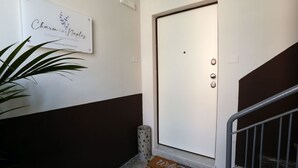 A hotel entrance with a white door, a welcome mat, a potted plant, and a sign above the door. - VivimiHome - CharmiNapoli Chiaia Room (Naples)