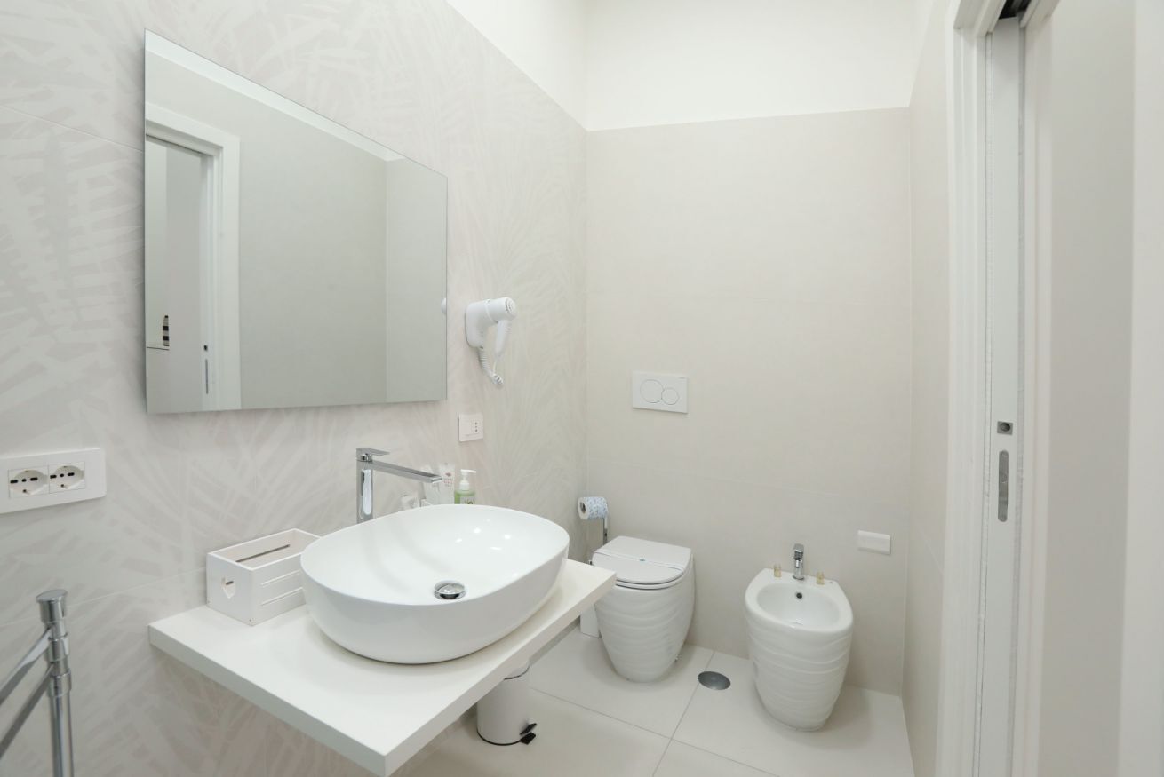 Un baño moderno con un lavamanos grande de color blanco, un espejo, un inodoro y un bidé.