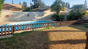 A swimming pool with a wooden fence, surrounded by grass and trees. - Chalet Villa Antonia (Ayamonte)