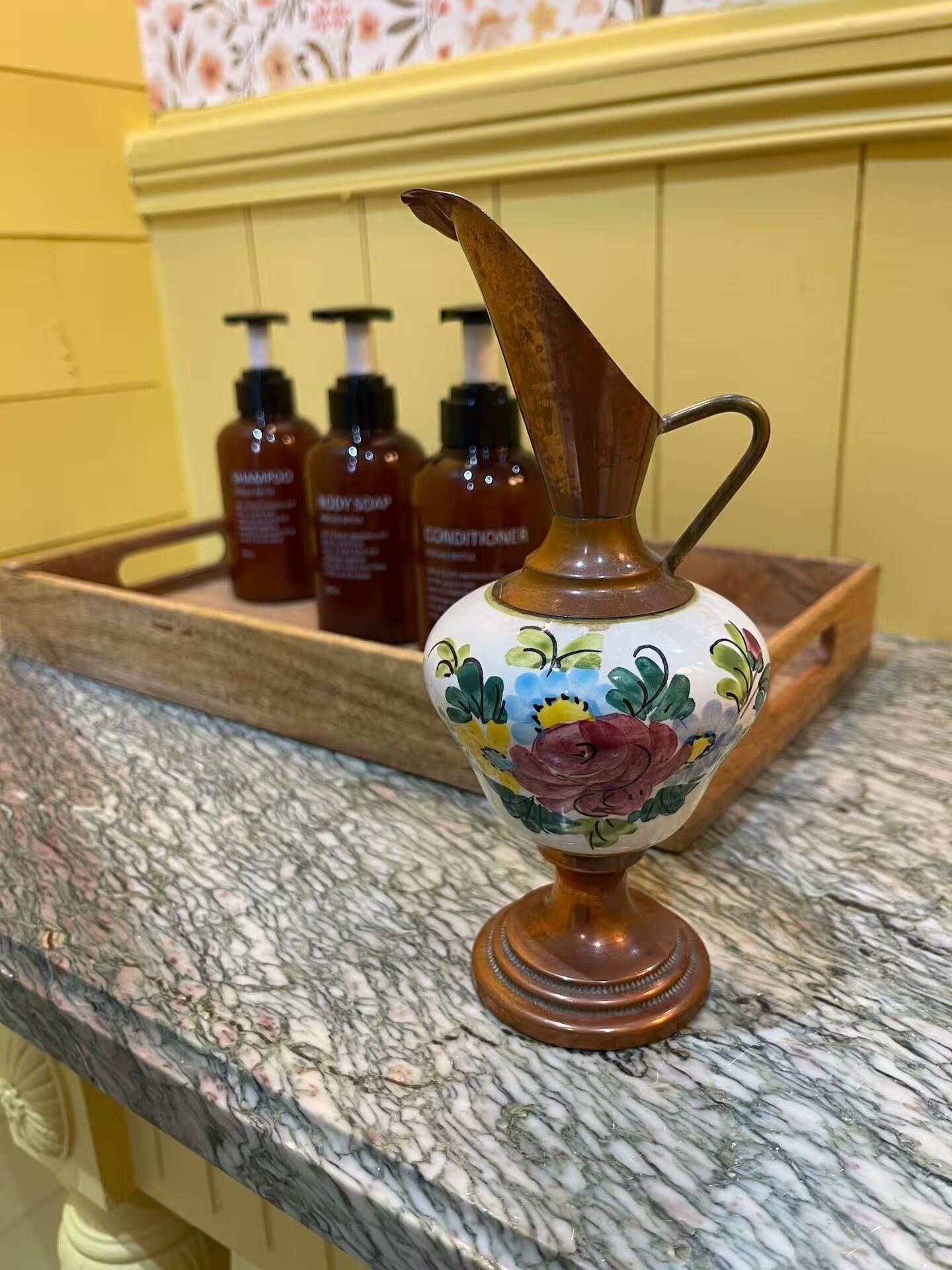 A marble countertop with a decorative ceramic pitcher and three bottles of body soap in the background.