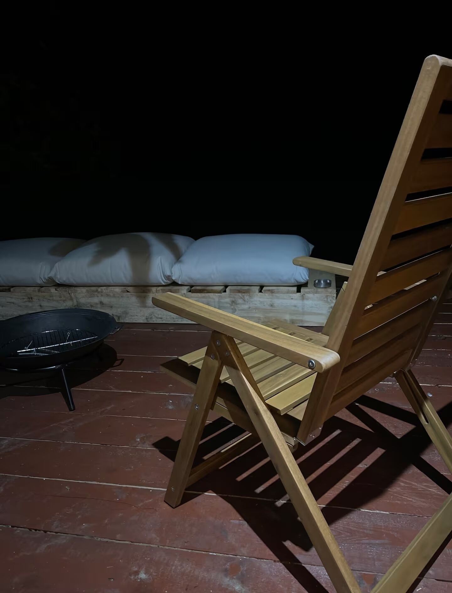 A wooden chair with a backrest and armrests, positioned on a tiled patio.