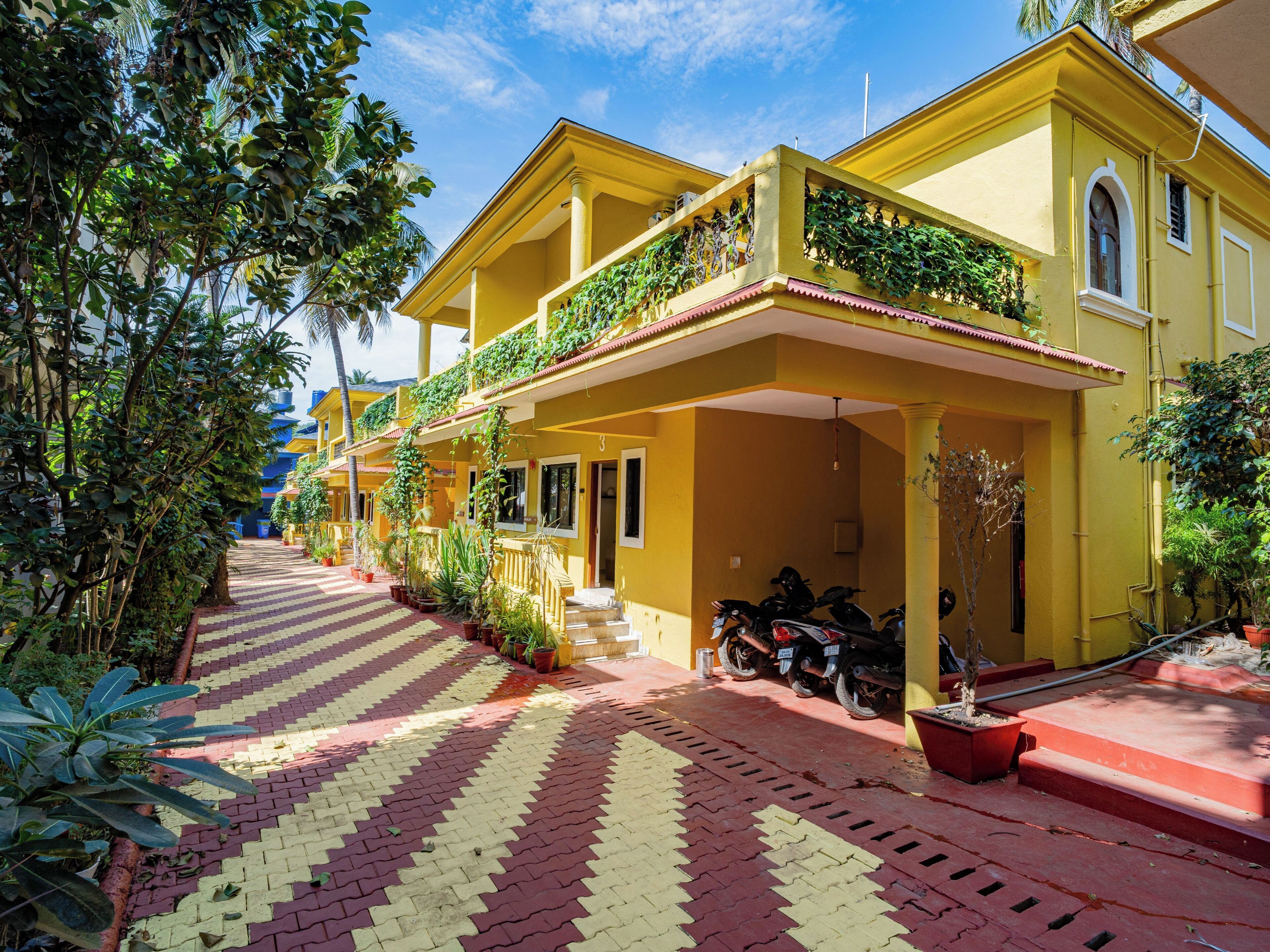 Un bâtiment jaune avec une allée couverte, des plantes en pot et des motos garées.