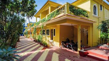 Un bâtiment jaune avec une allée couverte, des plantes en pot et des motos garées.