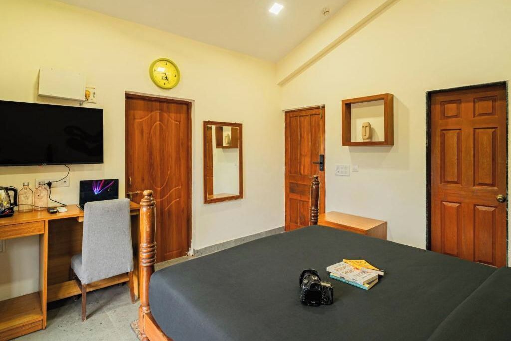 A bedroom with a bed, a desk, a chair, a television, a clock, and a door.