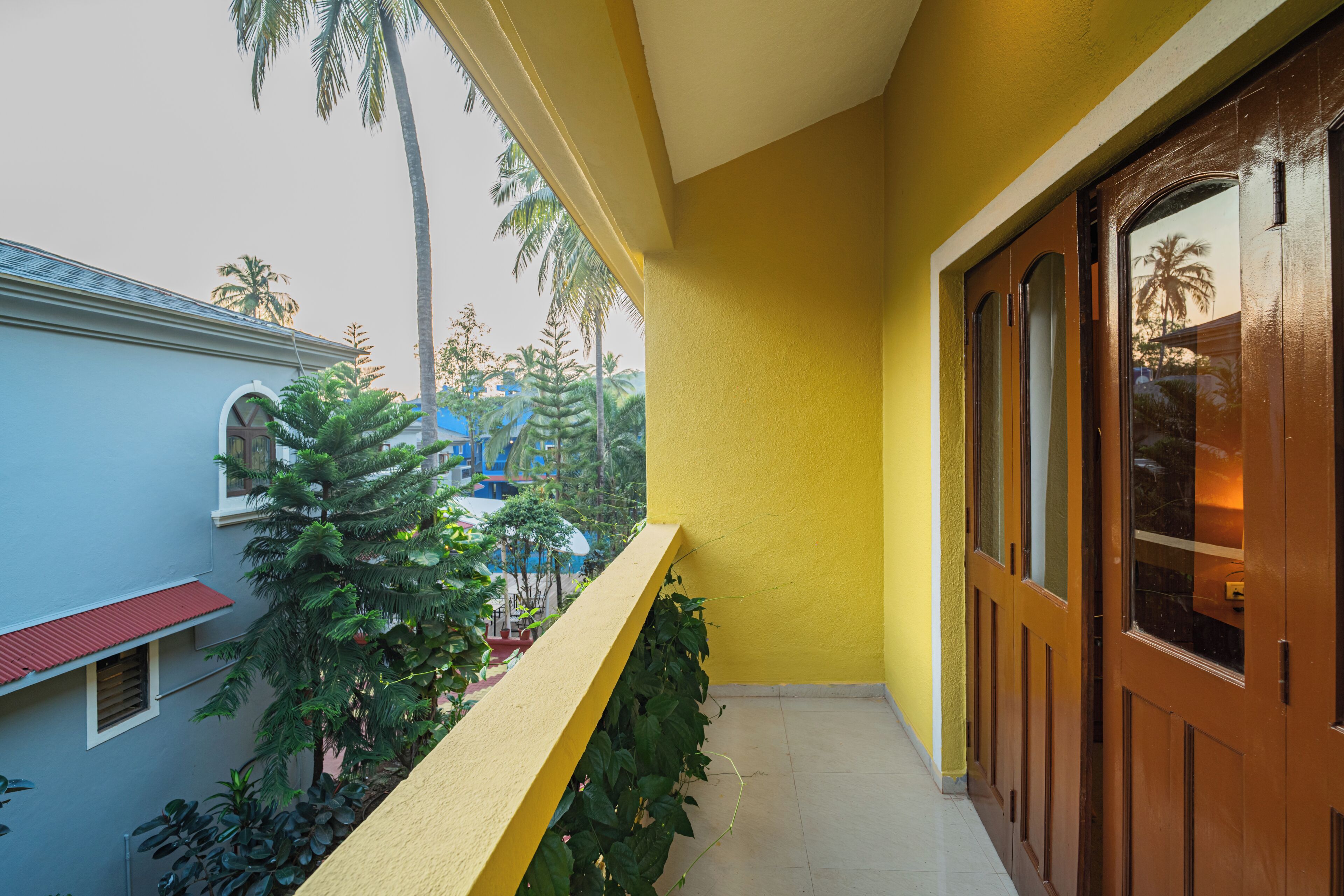 A yellow exterior wall with a wooden door and a balcony with plants.