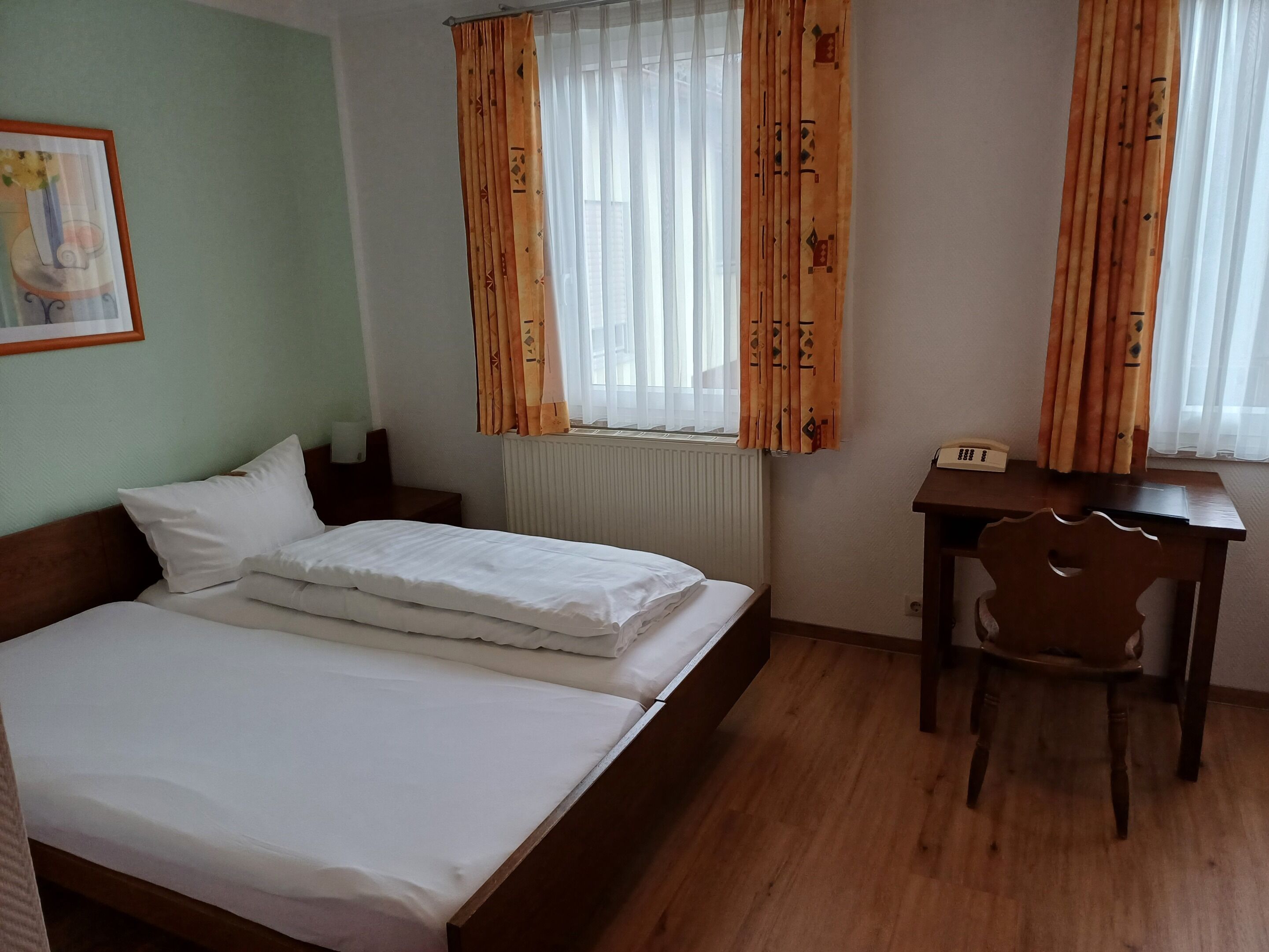 Una habitación de hotel con una cama doble, un escritorio de madera, una silla, un radiador y cortinas.