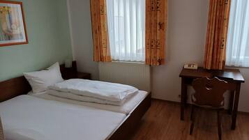 Una habitación de hotel con una cama doble, un escritorio de madera, una silla, un radiador y cortinas.