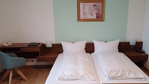 Un lit double avec du linge de lit blanc, une table de chevet avec une lampe, une chaise et un tableau au mur.