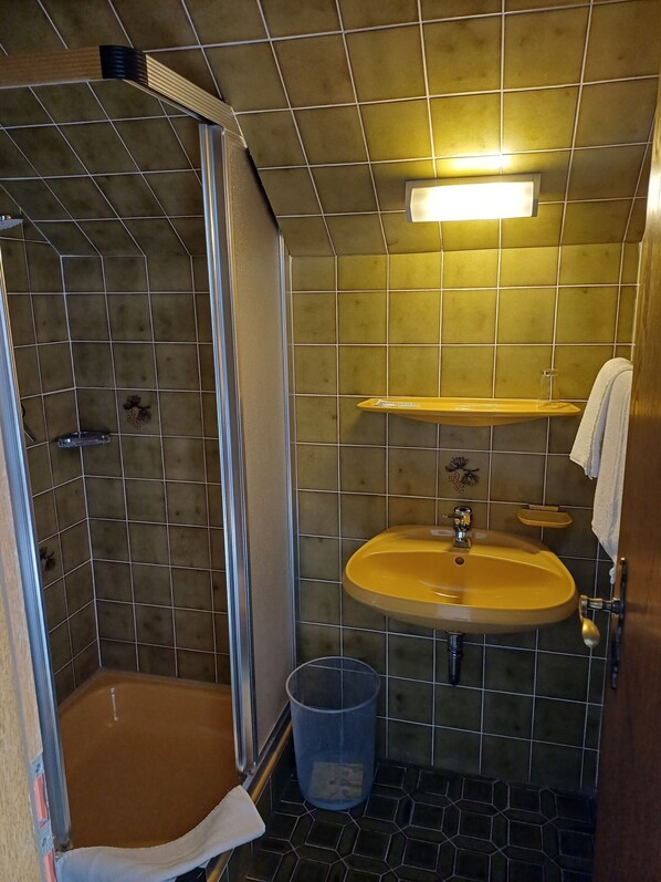 A small bathroom with a shower, a sink, and a trash can.