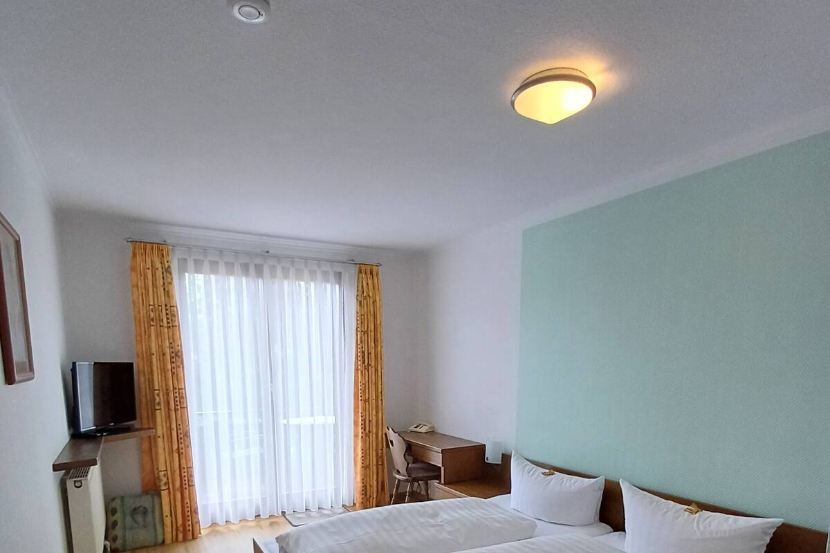 A hotel room with a double bed, a desk with a chair, a television, and a window with curtains.