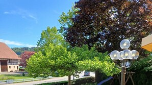 Un sentier pavé de pierres mène à un espace extérieur aménagé avec des tables et des chaises, entouré de verdure et sous un ciel dégagé.