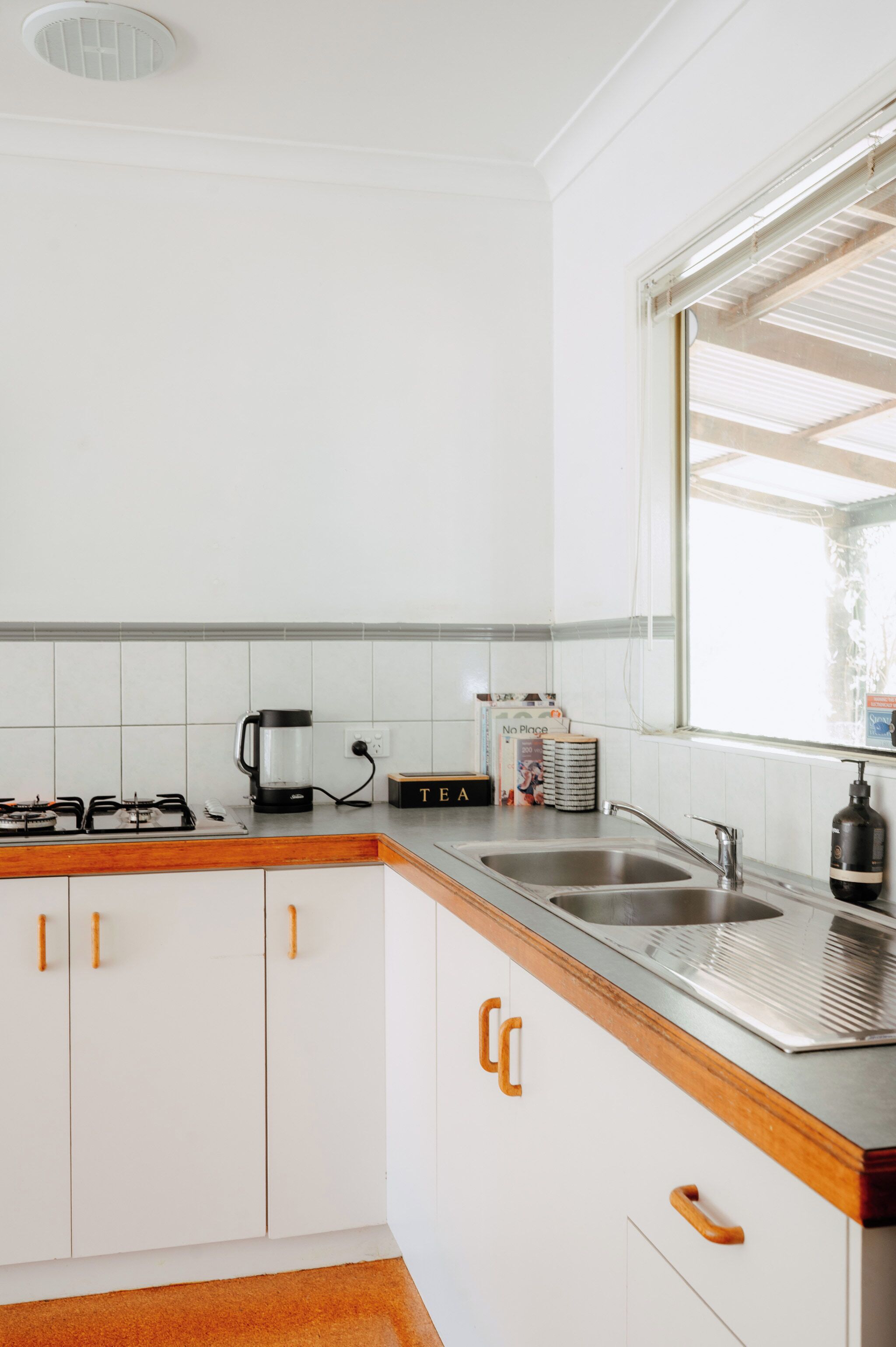 A kitchen with white cabinets, a gas stove, a coffee maker, and a window with blinds.