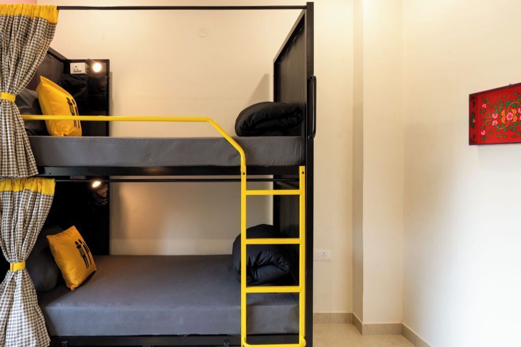 Habitación con literas, una escalera amarilla, almohadas negras y amarillas, y un cuadro rojo en la pared.