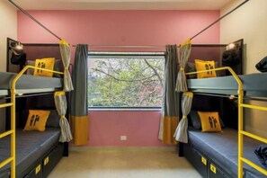 Une chambre de dortoir avec des lits superposés, des rideaux et une fenêtre donnant sur des arbres.