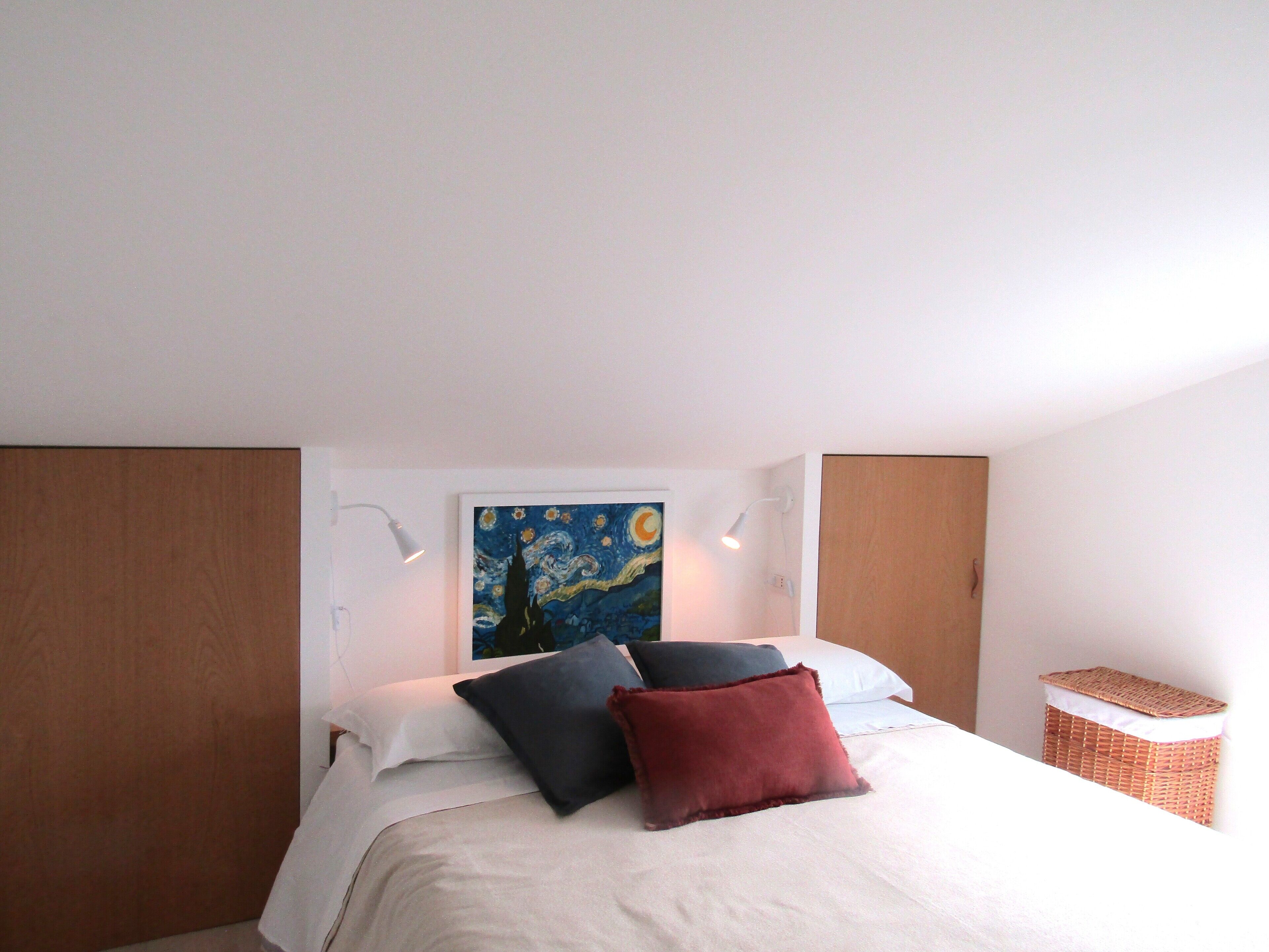 A bedroom with a bed, a painting on the wall, and a nightstand.