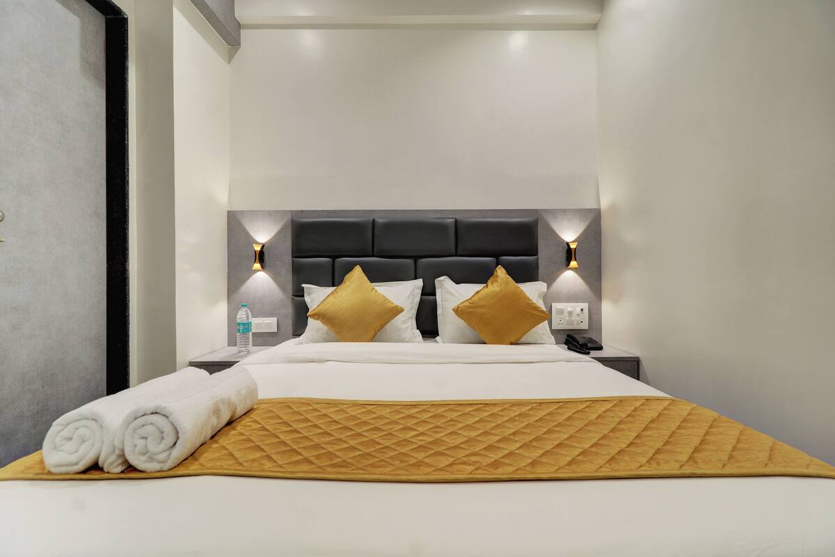 Ein ordentlich bezogenes Bett mit einer gesteppten Decke, zwei goldenen Kissen und einem Nachttisch mit einer Wasserflasche und einem Telefon.