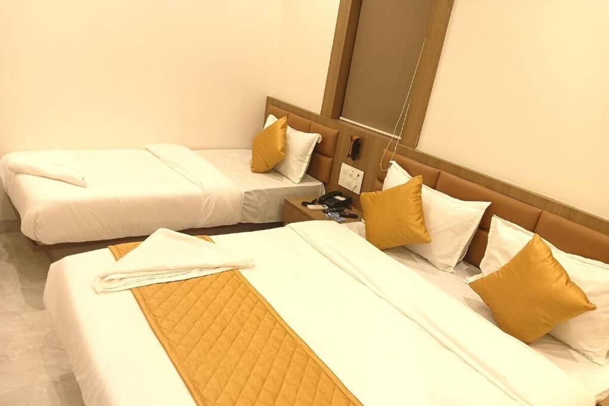 Ein Hotelzimmer mit zwei Einzelbetten, jeweils mit weißer Bettwäsche und goldenen Quilt-Akzenten.