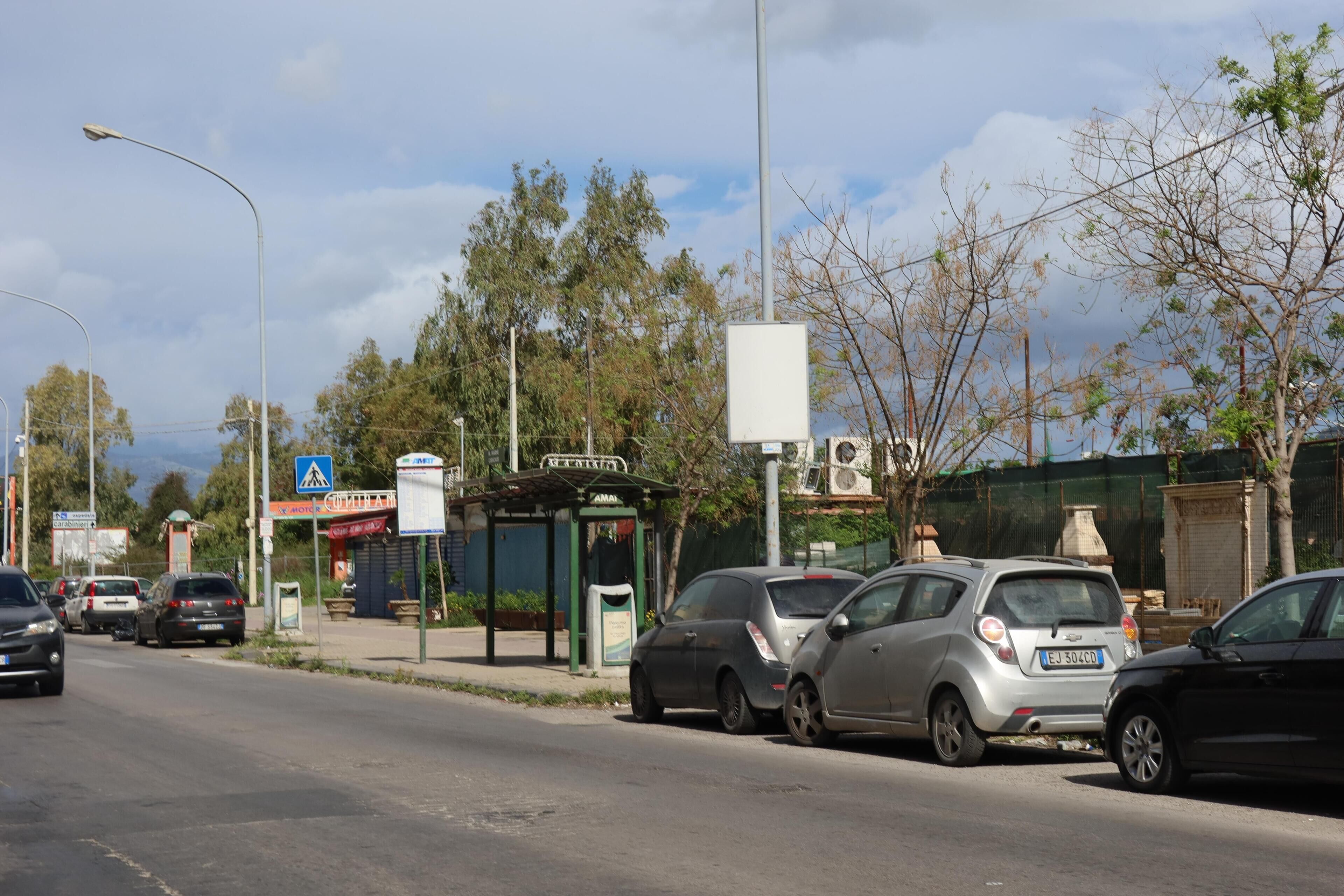 A street scene with parked cars, a bus stop, and a building with a sign.