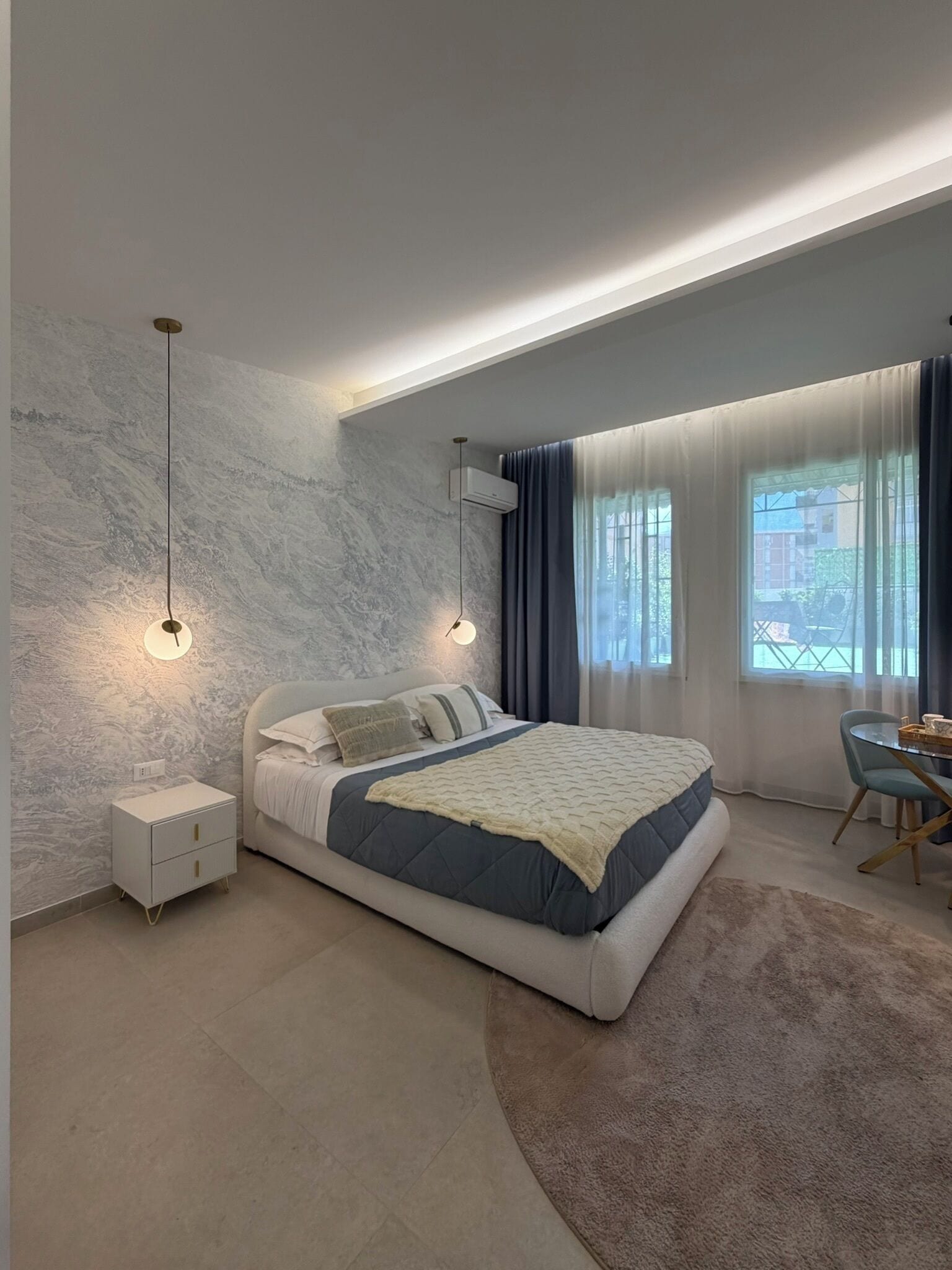 A modern bedroom with a bed, bedside tables, and a desk with chairs.
