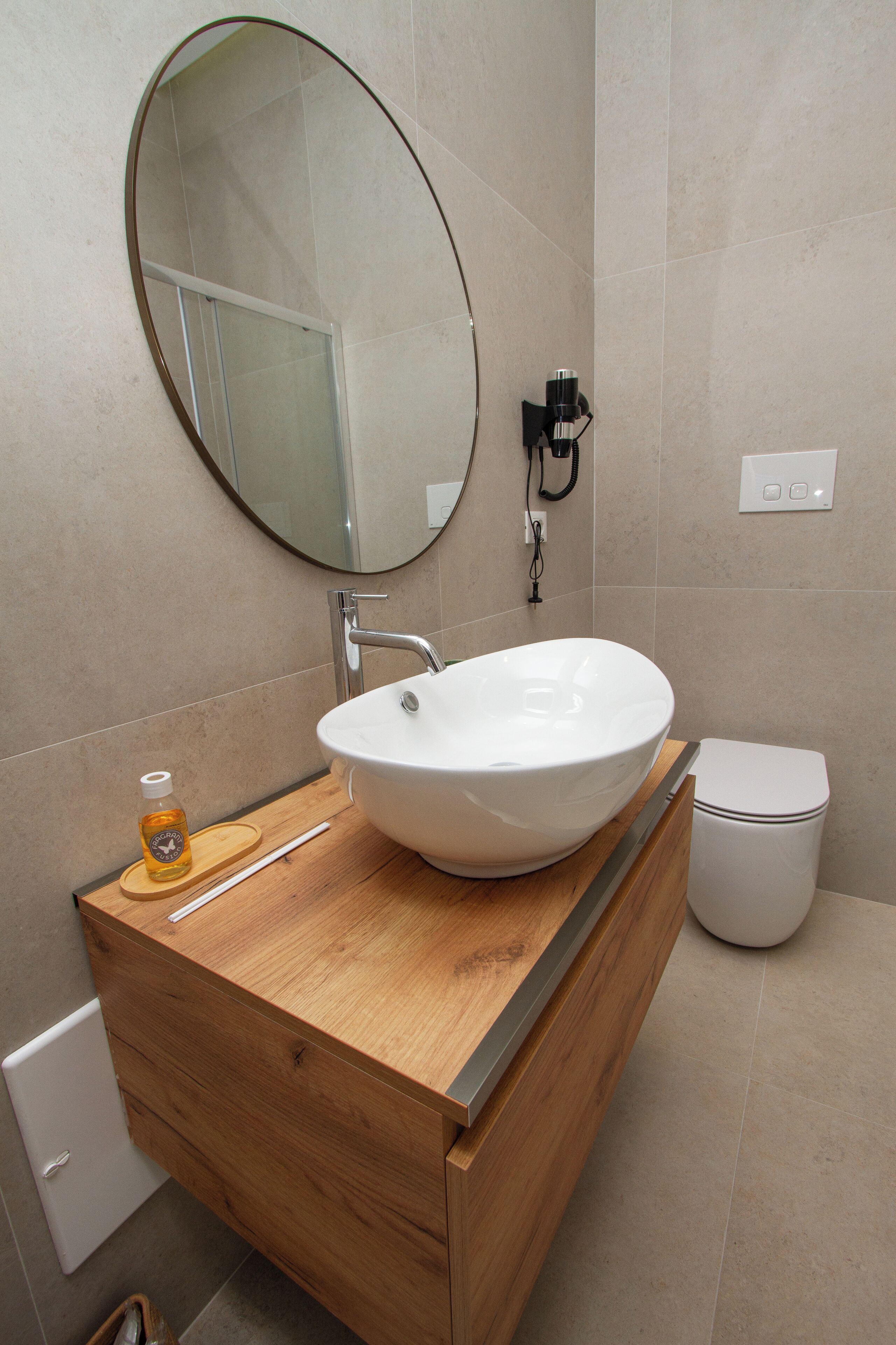 A bathroom with a wooden vanity, a white sink, a round mirror, and a toilet.
