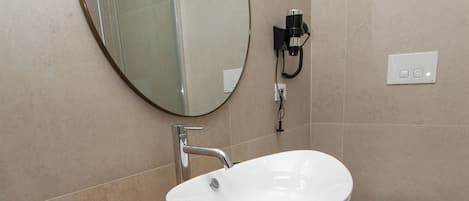 A bathroom with a wooden vanity, a white sink, a round mirror, and a toilet.