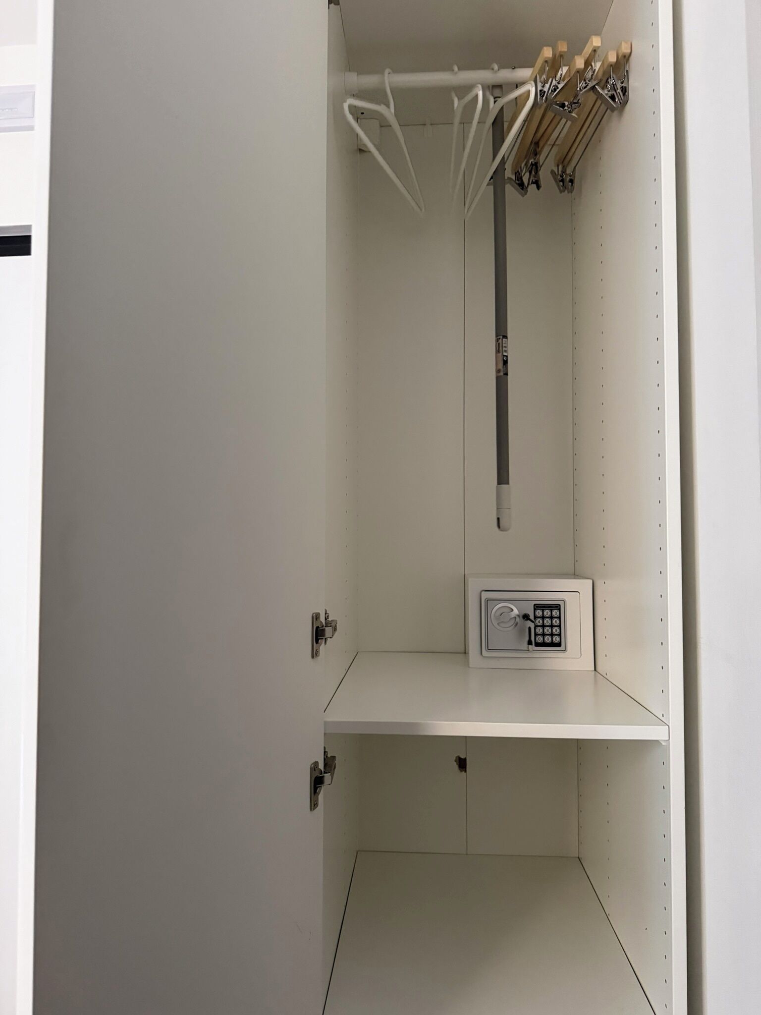 Ett vitt förvaringsskåp med ett inbyggt kassaskåp, en metallstång och en upphängningsanordning.
