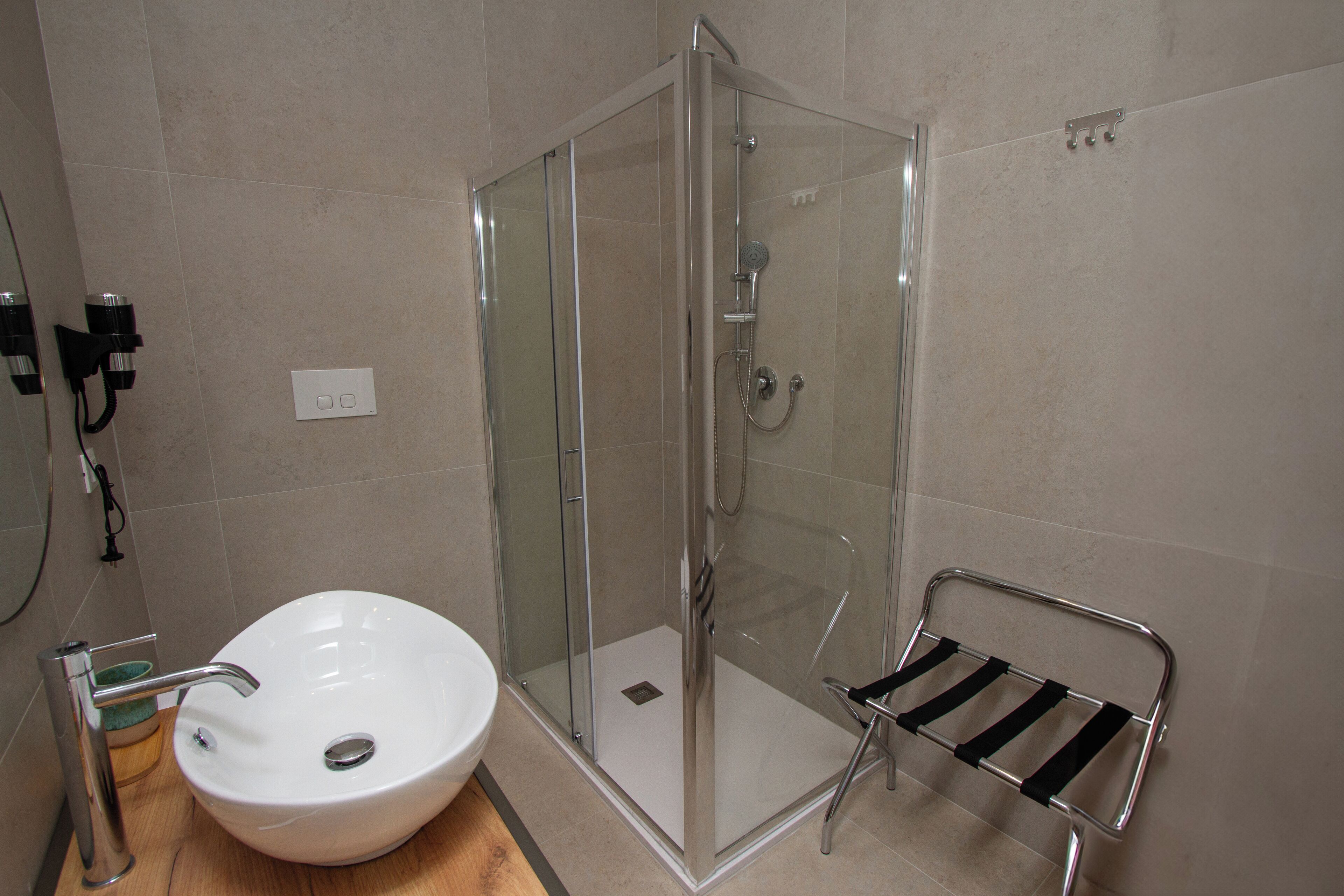 Un baño con ducha de vidrio, lavamanos blanco y un perchero para toallas.