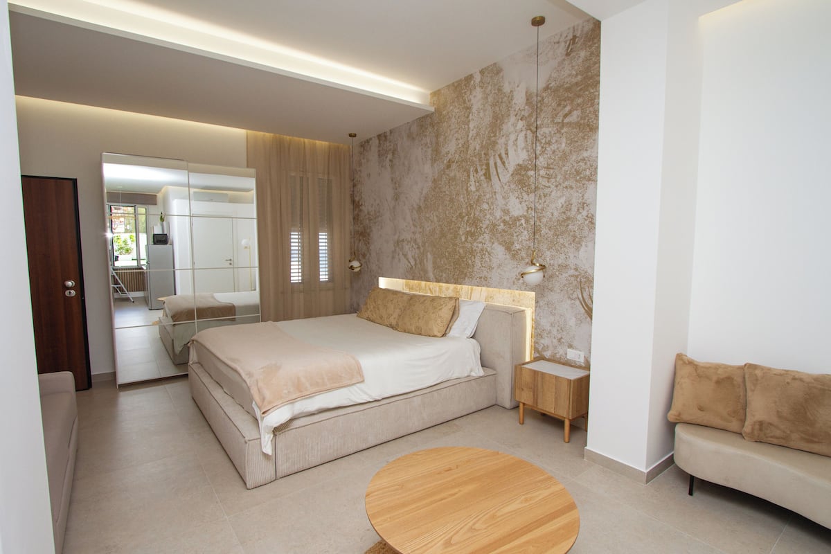 A modern bedroom with a large bed, bedside tables, a round wooden table, and a sofa.
