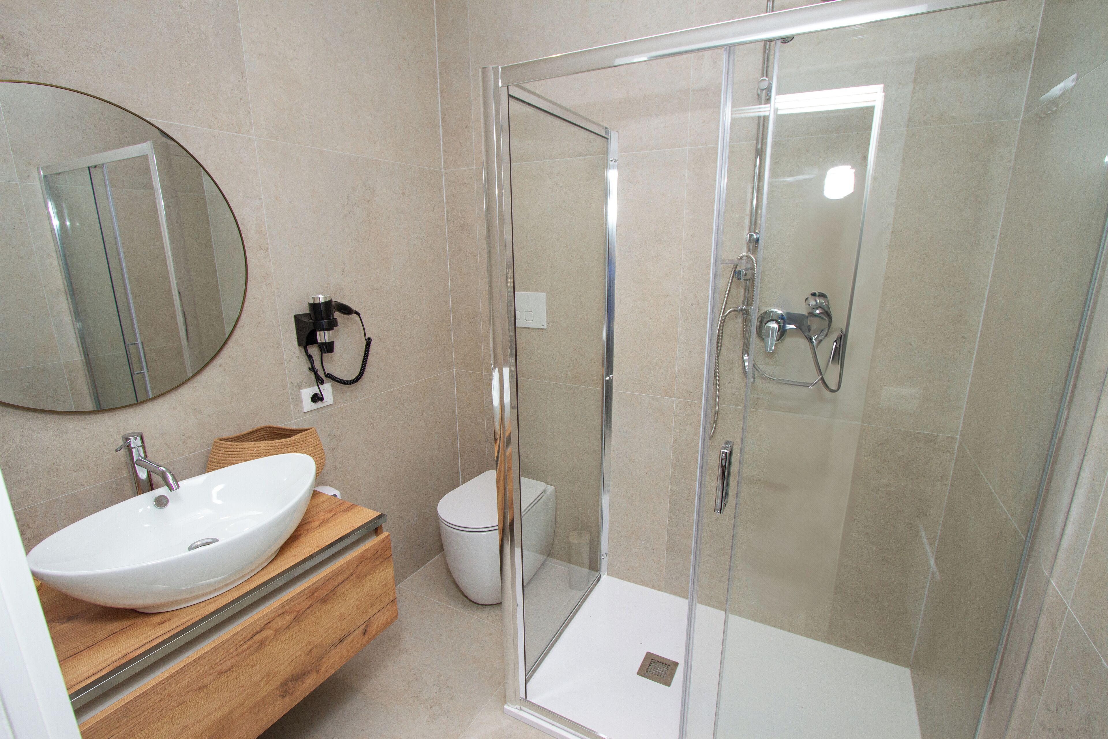 A modern bathroom with a glass-enclosed shower, a white sink, and a wooden vanity.