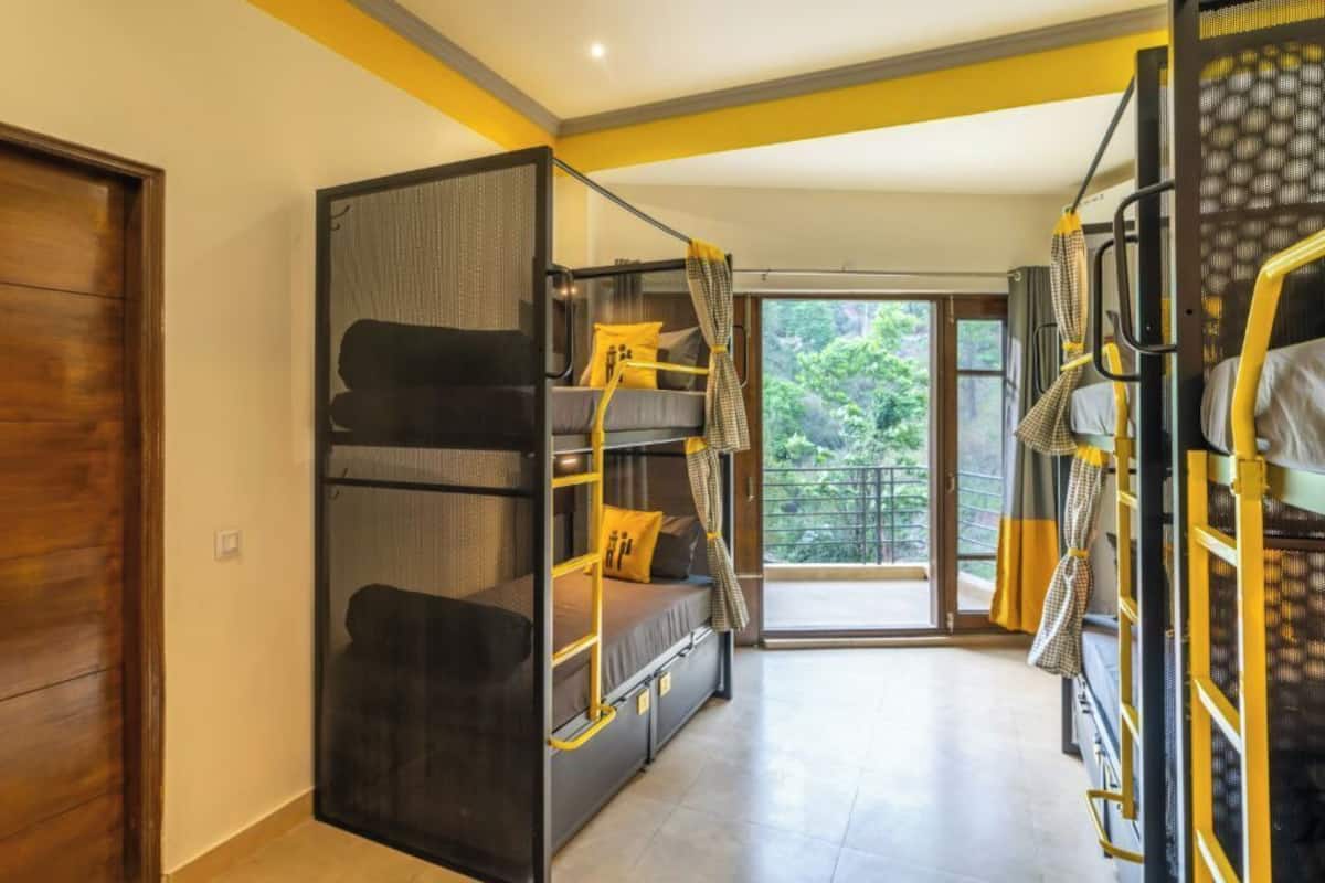Une chambre de dortoir avec des lits superposés, une porte coulissante donnant sur un balcon et une vue sur la verdure environnante.
