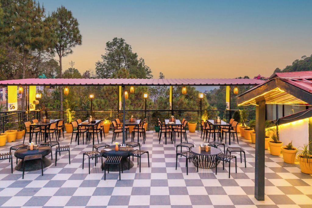 An outdoor dining area with checkered flooring, multiple tables and chairs, and string lights.