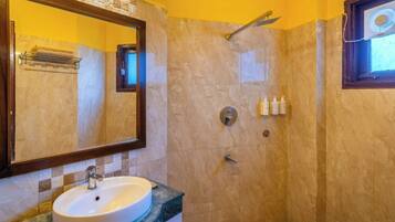 Un baño con lavamanos, espejo, ducha y artículos de aseo.