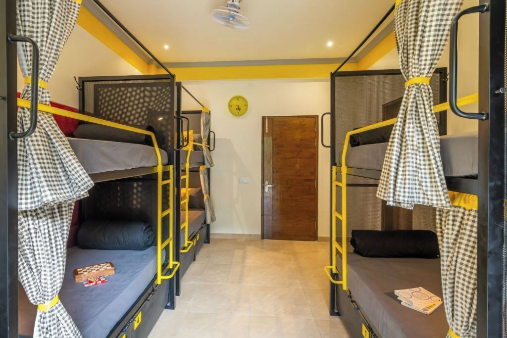 A dormitory room with bunk beds, a clock on the wall, and a door in the background.