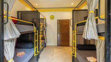 A dormitory room with bunk beds, a clock on the wall, and a door in the background.