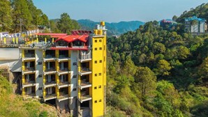 A multi-story hotel with balconies, a red-roofed structure, and a mountainous backdrop. - The Hosteller Kasauli (Kasauli)