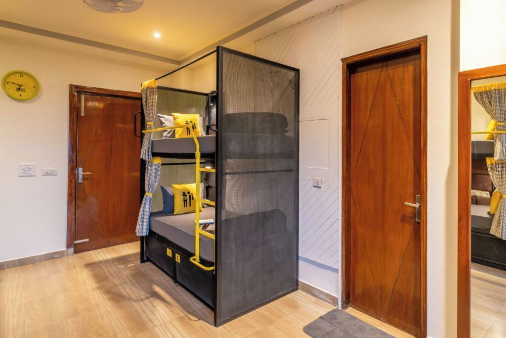 Una habitación con literas, una puerta de madera, un reloj y una vista parcial de otra habitación.