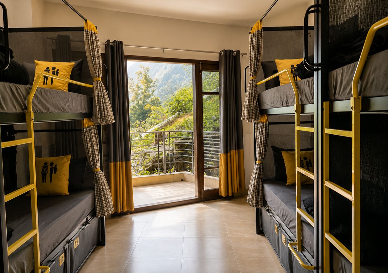 A dormitory room with bunk beds, a sliding glass door to a balcony, and curtains.