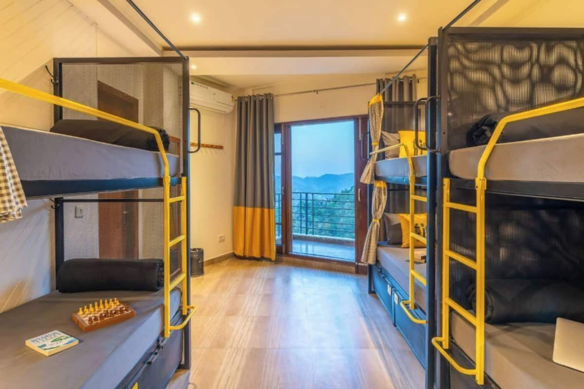 Une chambre de dortoir avec des lits superposés, un jeu d’échecs et une vue sur les montagnes par la fenêtre.
