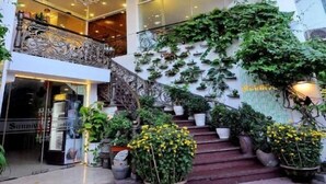 A hotel entrance with a grand staircase, a chandelier, and lush greenery.