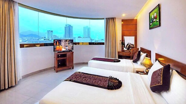A hotel room with two beds, a television, a city view, and a large window.