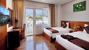 A hotel room with two beds, a desk, a chair, a TV, and a large window with a city view.