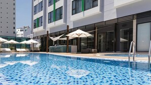A modern hotel with a swimming pool, outdoor seating, and a glass facade.