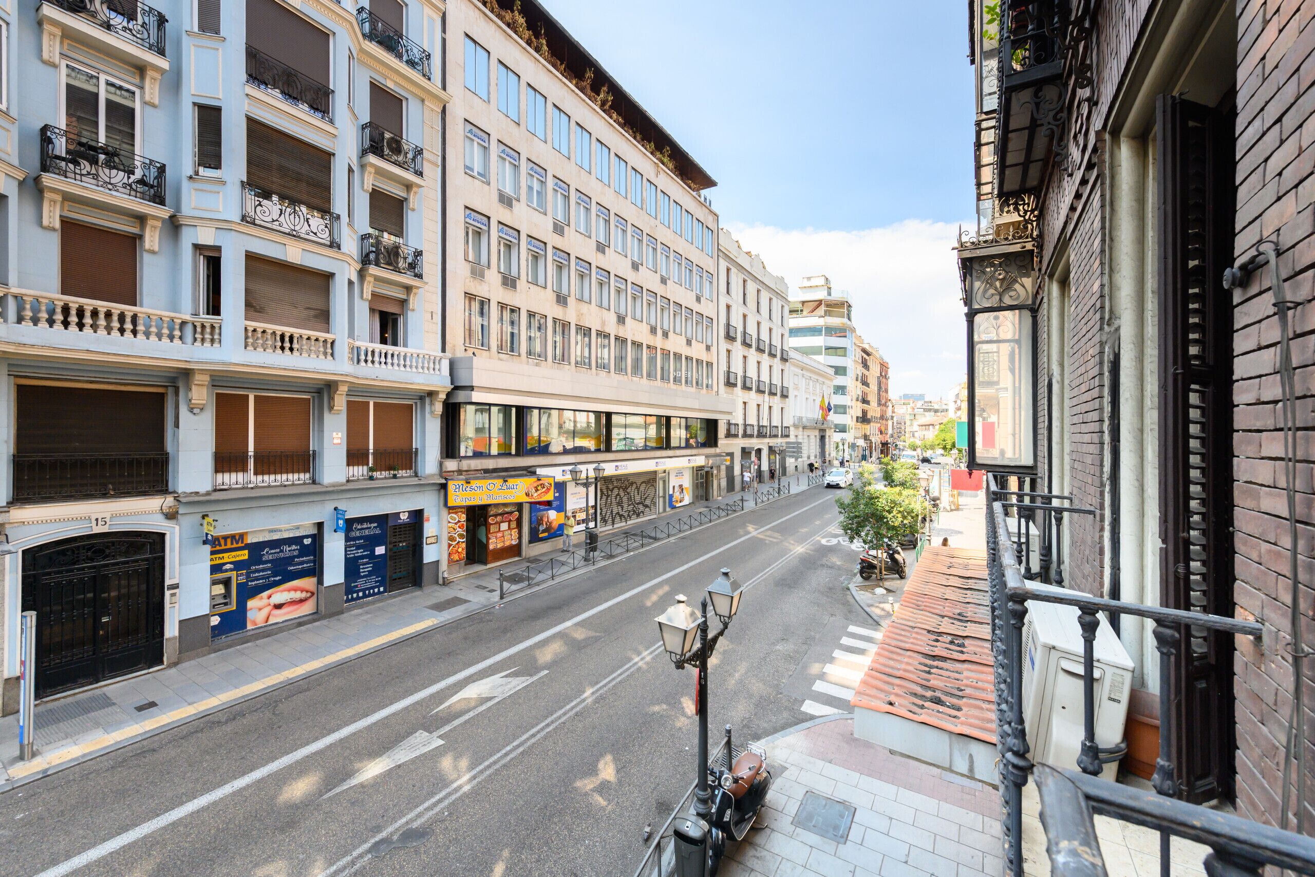 A street view with a building featuring multiple floors, balconies, and a storefront with advertisements.