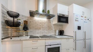 Una cocina moderna con armarios blancos, una campana extractora de acero inoxidable, un microondas integrado y un refrigerador con imanes.