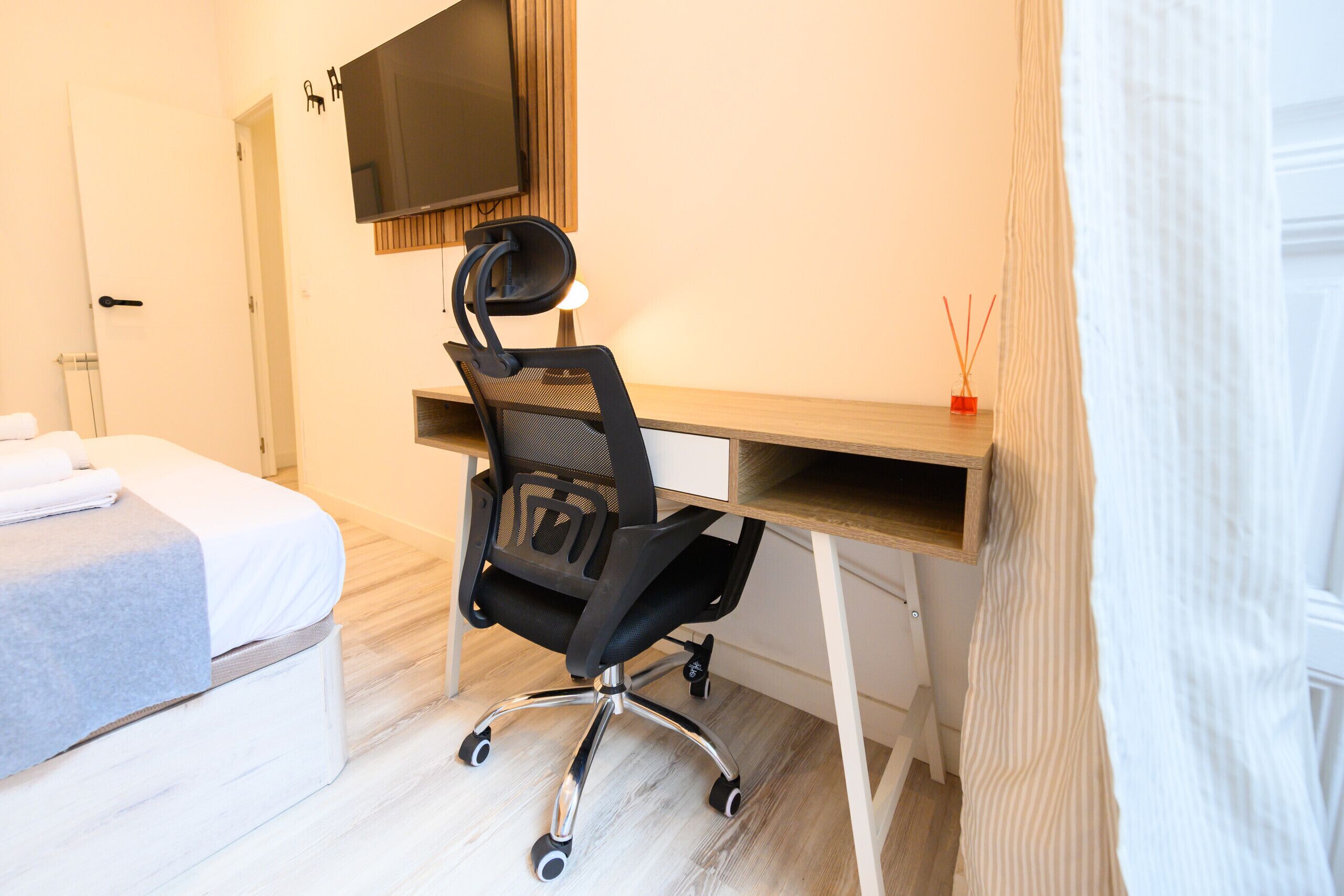 A hotel room with a bed, a desk with a chair, a television, and a small table with candles.