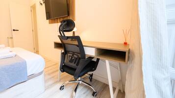 A hotel room with a bed, a desk with a chair, a television, and a small table with candles.